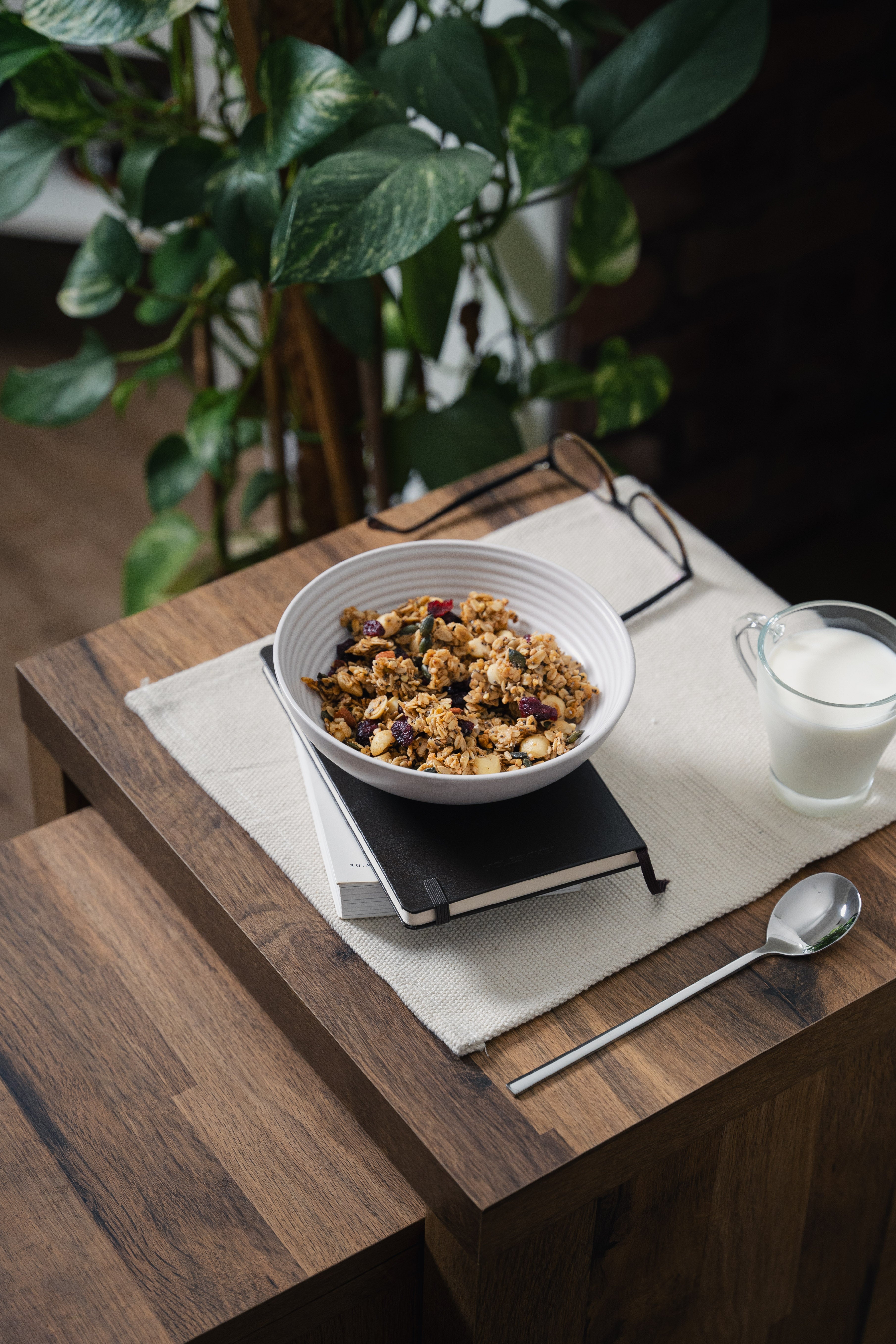 Nom Granola bowl breakfast scene with milk and a spoon on a wooden table 