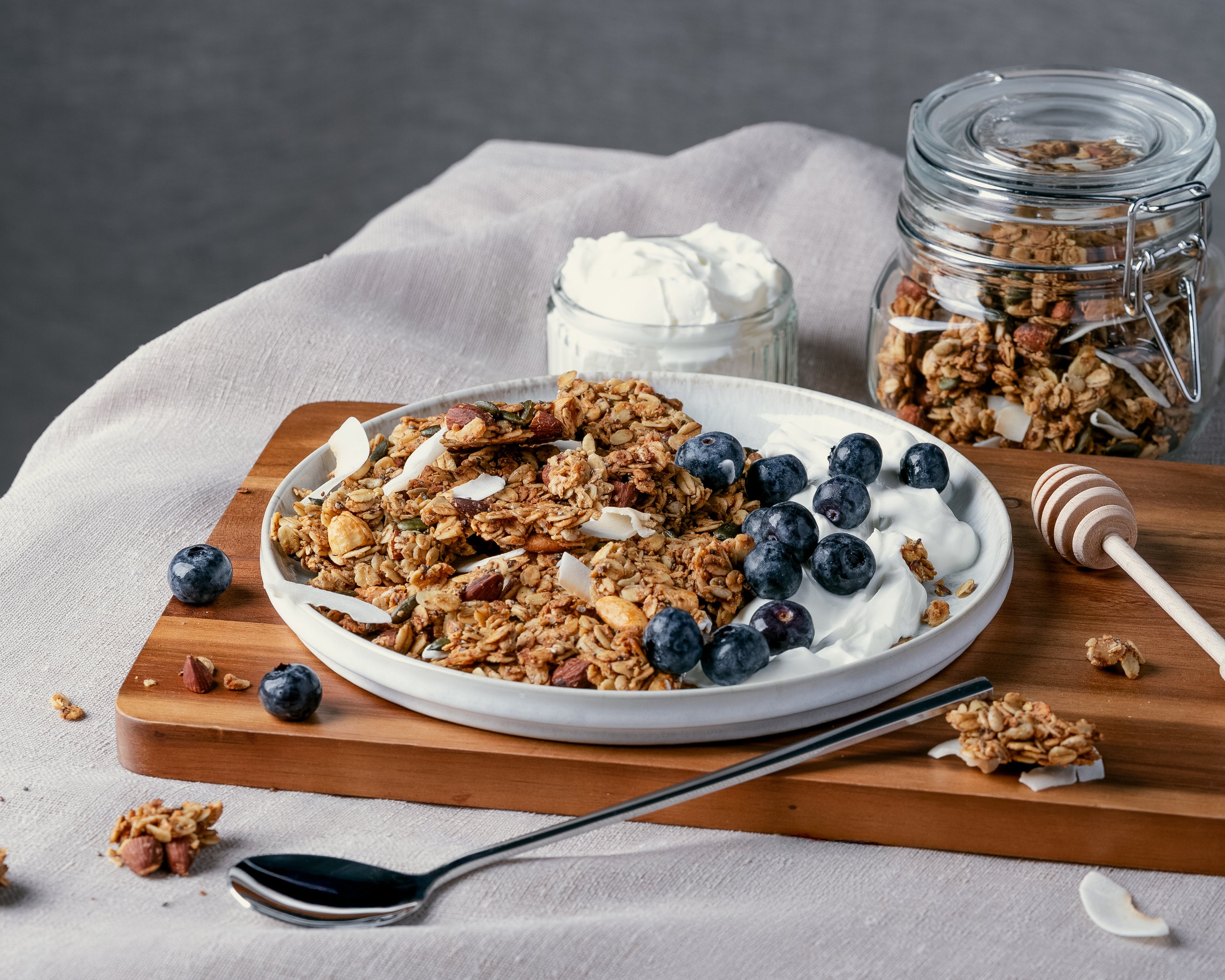 Nom Classic granola clusters with almonds cashews and coconut served on a plate with yogurt and fresh blueberries 