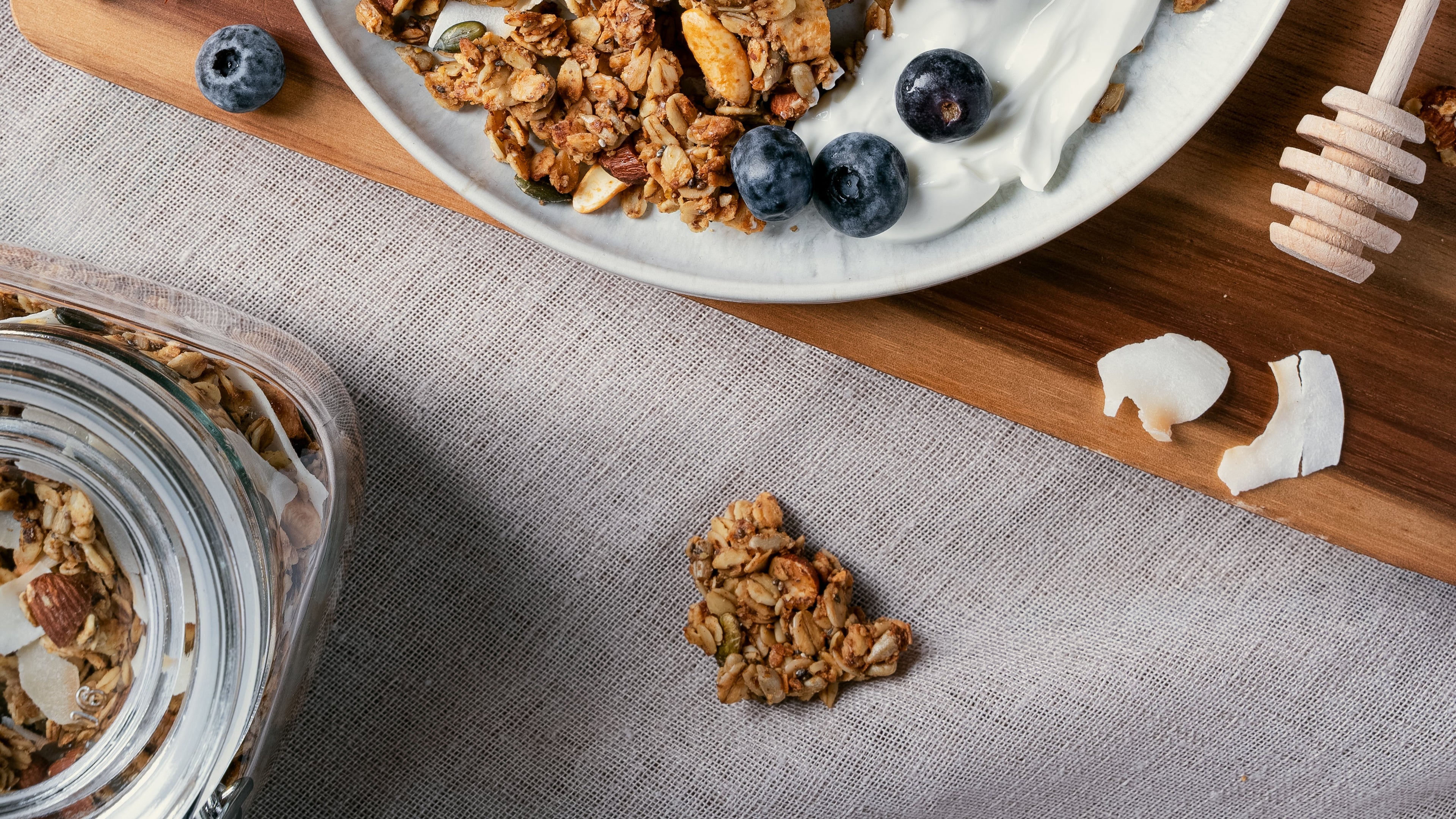 Nom Classic granola clusters with almonds cashews and coconut served on a plate with yogurt and fresh blueberries 