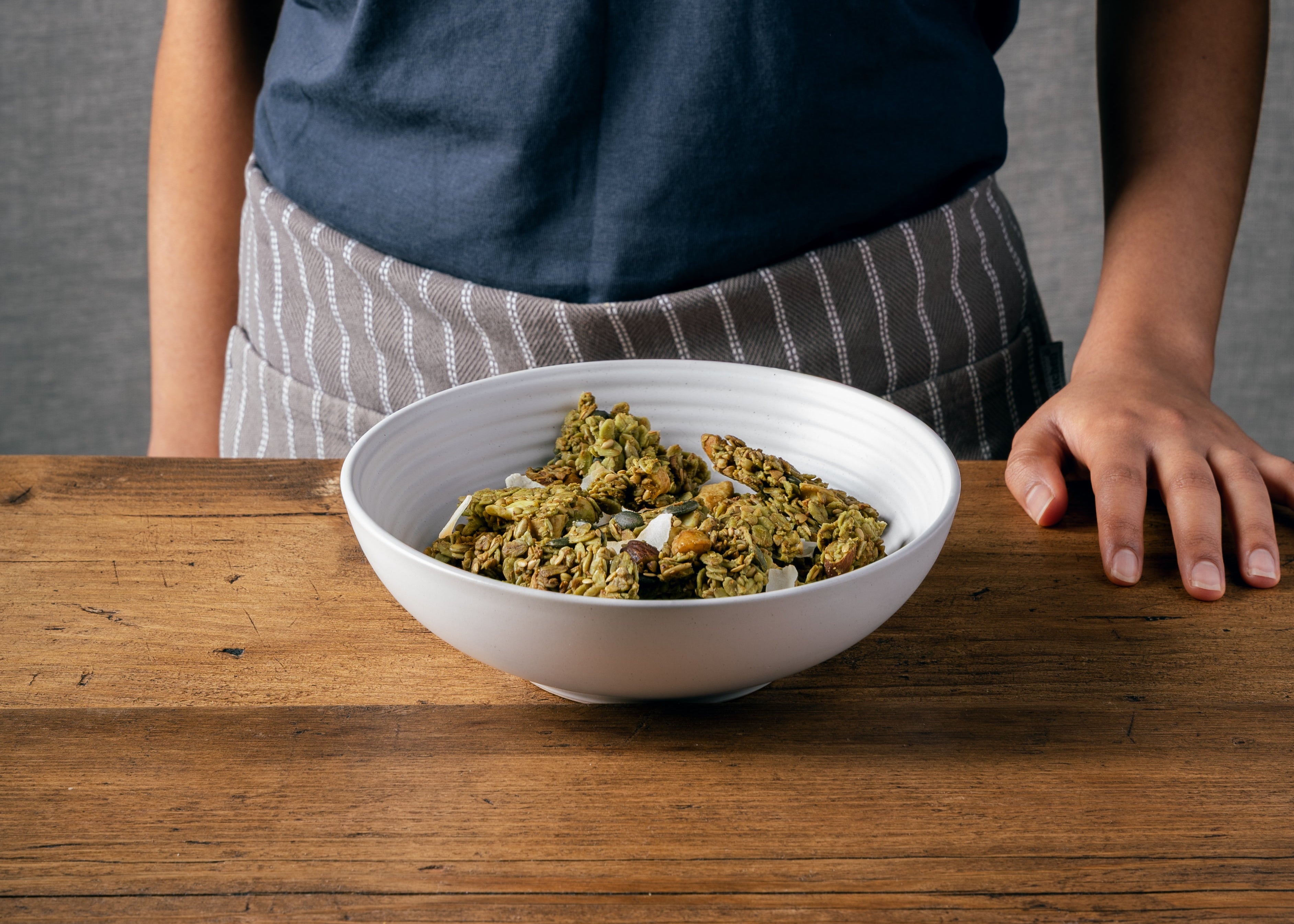 Matcha + Nut Granola clusters in a white bowl and the Nom Granola founder standing in the background