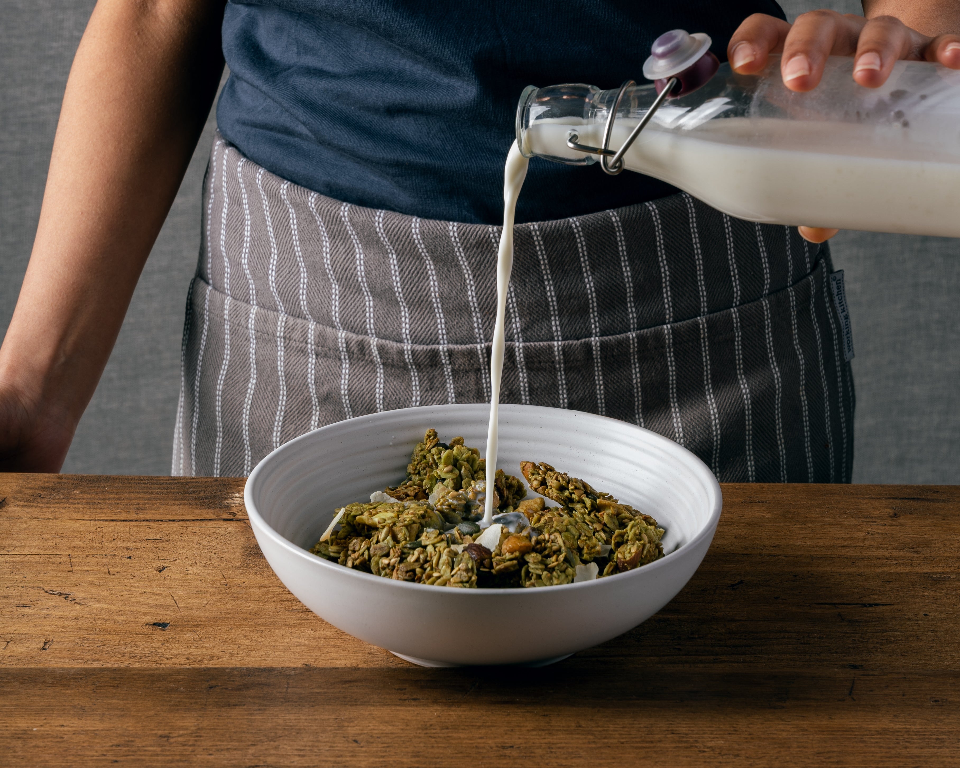 Fresh milk being poured over Matcha + Nut Nom Granola in a white ceramic bowl Leicester UK